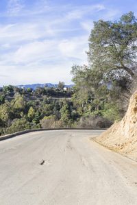 a paved road winding up to the top of a hill with trees on both sides and mountains beyond