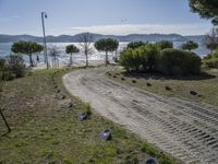 a road with stones between the grass and the water on the other side of it