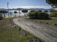 a road with stones between the grass and the water on the other side of it