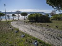 a road with stones between the grass and the water on the other side of it