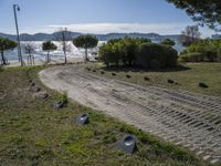 a road with stones between the grass and the water on the other side of it