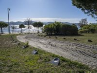 a road with stones between the grass and the water on the other side of it