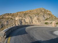 road in front of a rock mountain with some trees around it and a car parked in the driveway