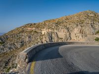 road in front of a rock mountain with some trees around it and a car parked in the driveway