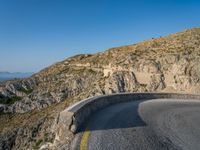 road in front of a rock mountain with some trees around it and a car parked in the driveway