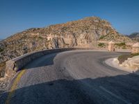 road in front of a rock mountain with some trees around it and a car parked in the driveway