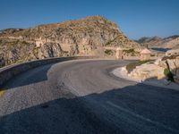 road in front of a rock mountain with some trees around it and a car parked in the driveway