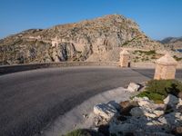 road in front of a rock mountain with some trees around it and a car parked in the driveway