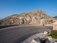 road in front of a rock mountain with some trees around it and a car parked in the driveway