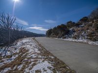 a road running along side a mountain covered with snow and grass covered in small, leafless grass