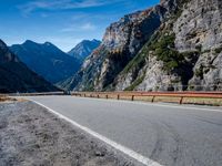 a road near mountains with cars going through it on a clear day in italy by a cliff