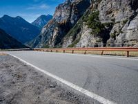 a road near mountains with cars going through it on a clear day in italy by a cliff