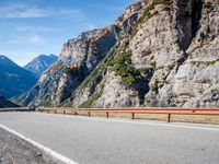 a road near mountains with cars going through it on a clear day in italy by a cliff