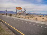 a road and sign are set on the side of a road with mountains in the distance