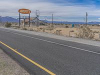 a road and sign are set on the side of a road with mountains in the distance