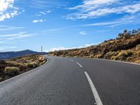 a winding highway curves with mountains in the distance and clouds above them that appear to be blue sky