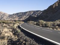 a paved road stretches into the mountains from a desert area with sparse vegetation and bushes