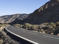 a paved road stretches into the mountains from a desert area with sparse vegetation and bushes