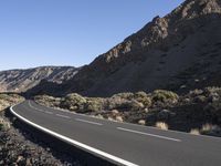 a paved road stretches into the mountains from a desert area with sparse vegetation and bushes