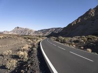 a paved road stretches into the mountains from a desert area with sparse vegetation and bushes