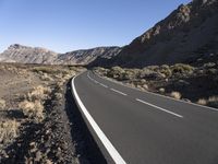 a paved road stretches into the mountains from a desert area with sparse vegetation and bushes