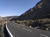 a paved road stretches into the mountains from a desert area with sparse vegetation and bushes