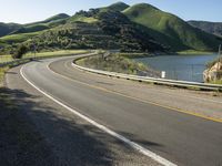 a road near a lake with hills in the background and water in the middle of a gravel road