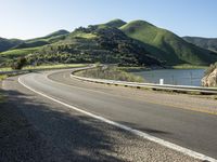 a road near a lake with hills in the background and water in the middle of a gravel road