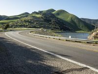 a road near a lake with hills in the background and water in the middle of a gravel road