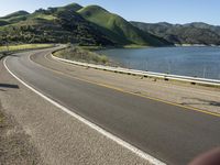 a road near a lake with hills in the background and water in the middle of a gravel road