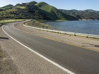 a road near a lake with hills in the background and water in the middle of a gravel road