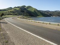 a road near a lake with hills in the background and water in the middle of a gravel road