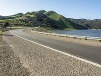 a road near a lake with hills in the background and water in the middle of a gravel road