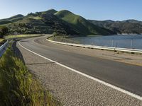 a road near a lake with hills in the background and water in the middle of a gravel road