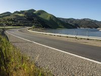 a road near a lake with hills in the background and water in the middle of a gravel road