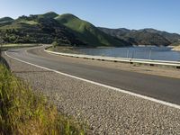 a road near a lake with hills in the background and water in the middle of a gravel road