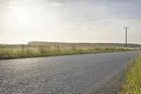 a man is riding a skateboard down the side of the road, near some tall grass