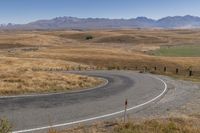 a road leading through dry grass hills with mountains in the background of the image,