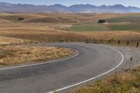 a road leading through dry grass hills with mountains in the background of the image,