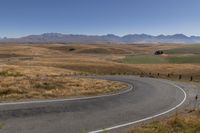 a road leading through dry grass hills with mountains in the background of the image,