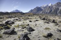 an expanse with rocks, grass and mountains in the background that appear to be about 50 percent in height of mountains