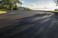 a tree lined park road with sun shining on the ground below it from a parking spot