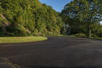 an empty road next to a forest on a hill side with grass and trees and a blue sky