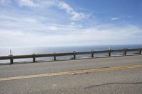 the road is very scenic by the ocean, and has an ocean and blue sky