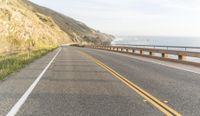 a yellow truck drives down a road near the ocean and cliffs with mountains in the background