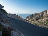 the road is winding past a cliff side area on a sunny day, with one car driving in the street