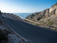 the road is winding past a cliff side area on a sunny day, with one car driving in the street