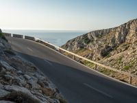 the road is winding past a cliff side area on a sunny day, with one car driving in the street