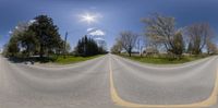 a fish eye lens view of a road that runs through the field and is partially filled with green grass and bushes