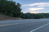 a motorcycle parked on the side of a highway near trees and a hill is seen from a moving vehicle